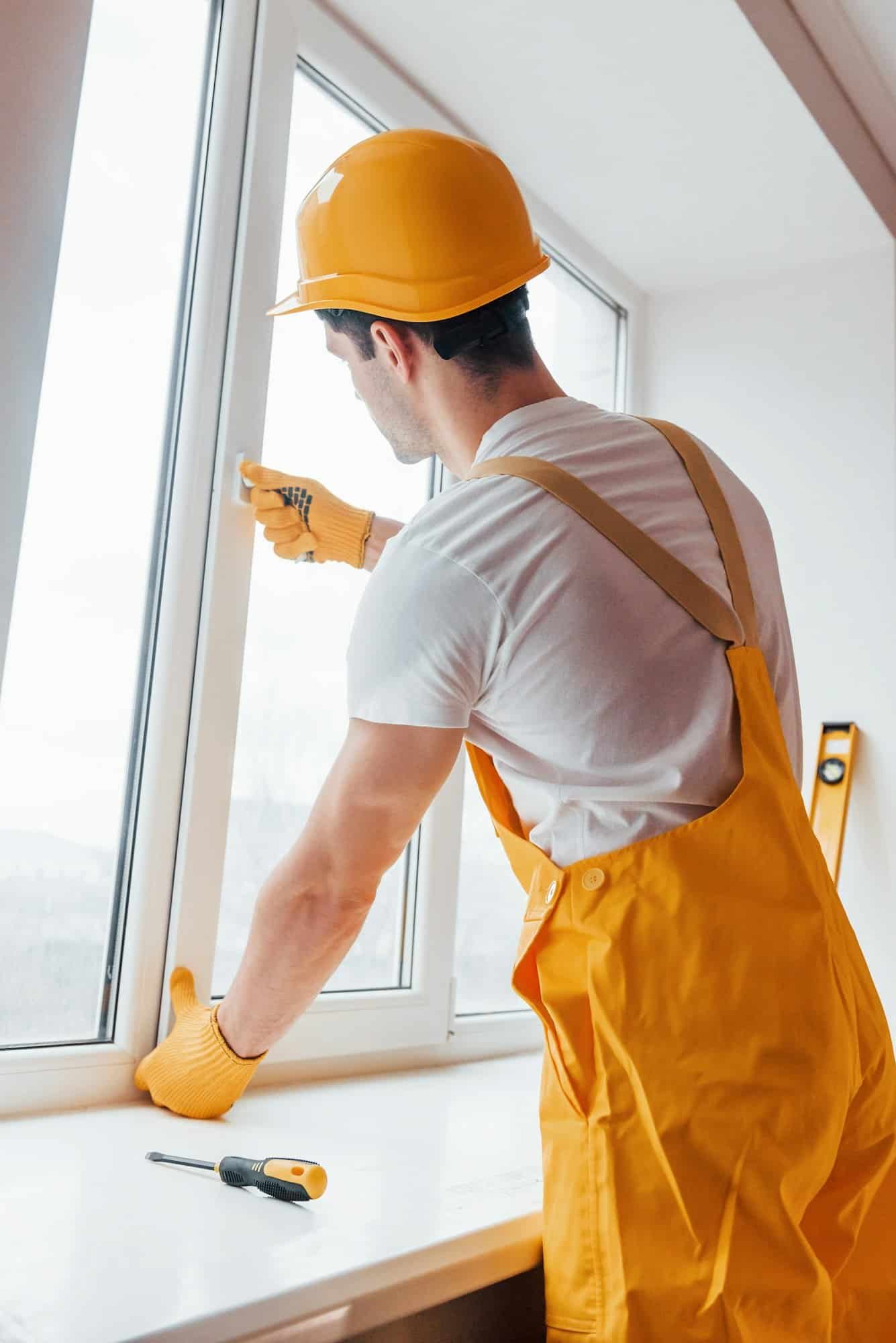 Handyman in yellow uniform installs new window. House renovation conception